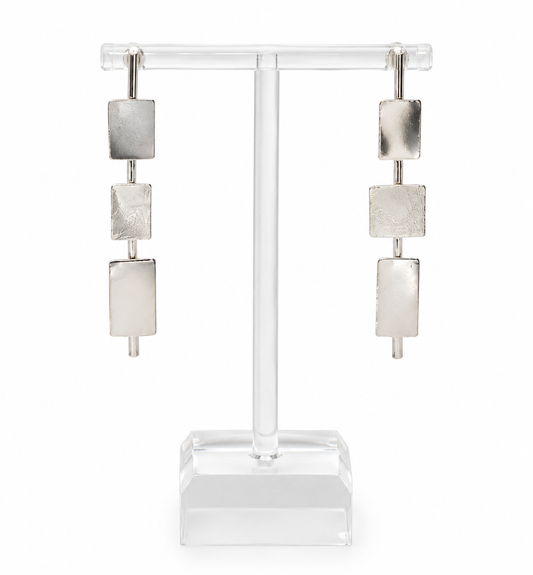Clarity sterling silver earrings with three geometric rectangular elements in varied textures and finishes, displayed on a clear acrylic jewelry stand.