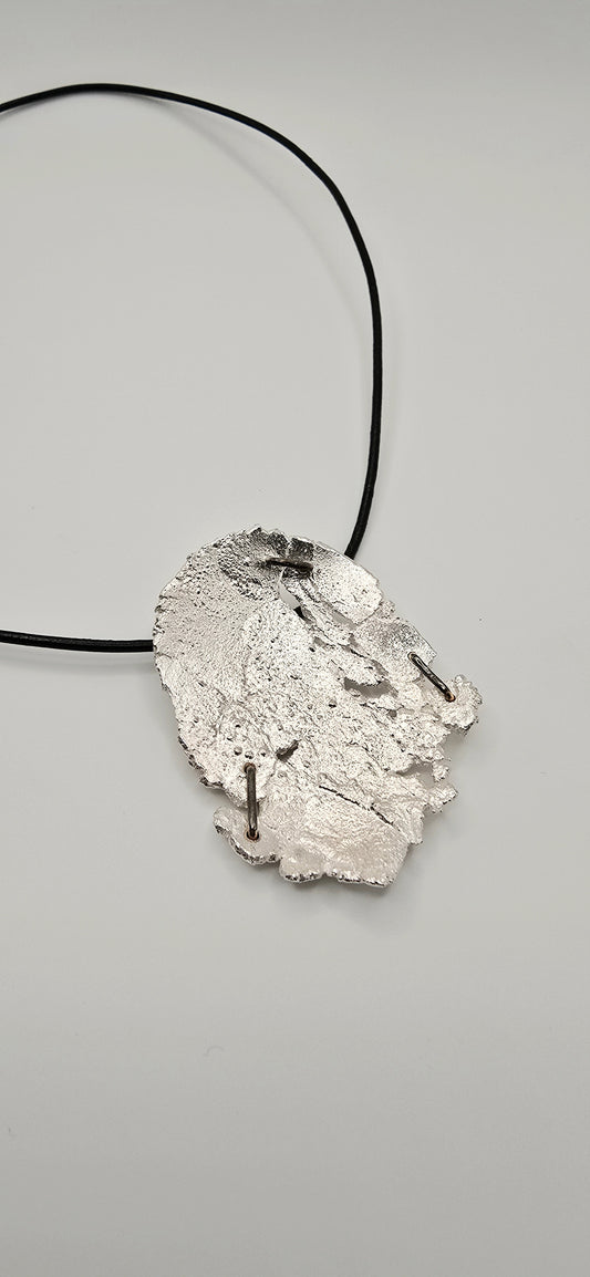 Sterling silver abstract pendant/ brooch with brass staples on a black leather cord against a gray background