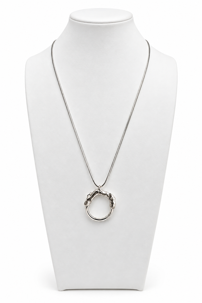 Melted and Modern sterling silver necklace displayed on a white jewelry bust, featuring a circular pendant with a textured molten silver upper form and smooth polished lower ring.