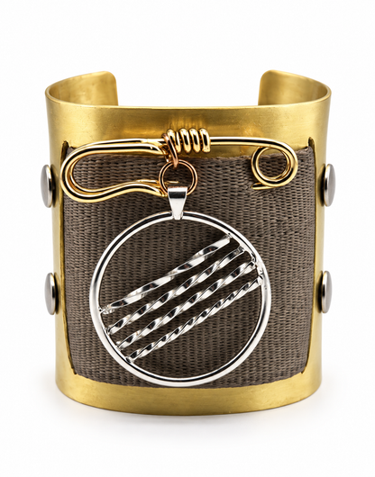 Front view of a one of a kind brass cuff bracelet with woven seat belt material, handcrafted brass safety pin, and large removable sterling silver pendant with diagonal textured detailing.